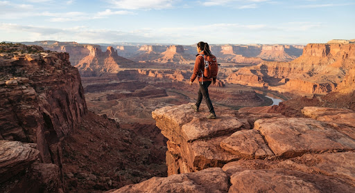 Hiker stepping out to scenic canyon precipice in Utah red rocks